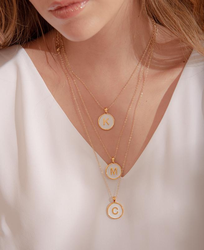 Imagen de la cadena con baño de oro con el dije redondo pintado a mano de color nude y con la letra F en dorado.