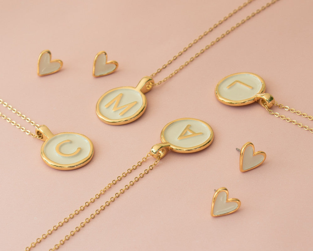 Imagen de la cadena con baño de oro con el dije redondo pintado a mano de color nude y con la letra en dorado.